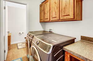 Laundry room with cabinets, light tile patterned floors, and washer and clothes dryer