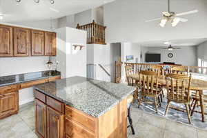 Kitchen with stone countertops, a center island, light tile patterned flooring, and a kitchen bar