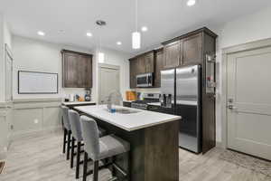 Kitchen with appliances with stainless steel finishes, decorative light fixtures, sink, dark brown cabinetry, and a center island with sink