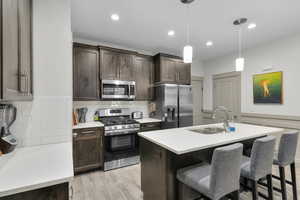 Kitchen featuring decorative light fixtures, sink, a kitchen island with sink, stainless steel appliances, and dark brown cabinets