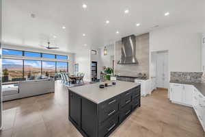 Kitchen with tasteful backsplash, a kitchen island, stove, wall chimney range hood, and white cabinets