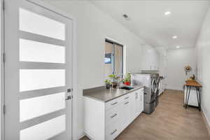 Washroom with sink, cabinets, washing machine and clothes dryer, and light wood-type flooring