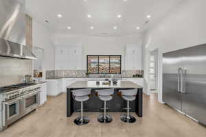 Kitchen with a kitchen island, white cabinetry, a kitchen bar, premium appliances, and wall chimney range hood