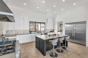 Kitchen featuring appliances with stainless steel finishes, white cabinetry, island range hood, a kitchen island, and decorative backsplash