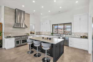 Kitchen featuring appliances with stainless steel finishes, white cabinetry, a center island, a kitchen bar, and wall chimney exhaust hood