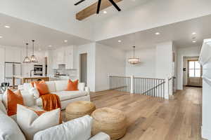 Living room with beam ceiling, light hardwood / wood-style flooring, and ceiling fan with notable chandelier