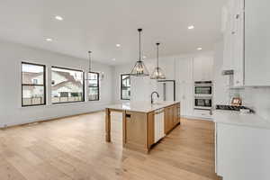 Kitchen featuring white cabinetry, hanging light fixtures, white appliances, and a spacious island