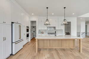 Kitchen with white cabinetry, high end white refrigerator, sink, a kitchen bar, and a spacious island