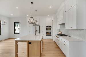 Kitchen with white cabinetry, decorative light fixtures, white double oven, built in fridge, and a kitchen island with sink