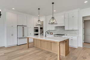 Kitchen with white appliances, sink, a kitchen island with sink, and white cabinets