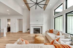 Living room featuring a tiled fireplace, beam ceiling, light hardwood / wood-style floors, and a towering ceiling