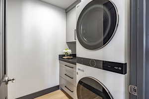 Laundry room featuring cabinets, stacked washer / drying machine, and light hardwood / wood-style floors