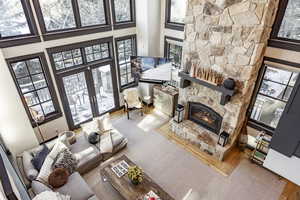 Living room featuring a high ceiling, a stone fireplace, carpet flooring, and french doors