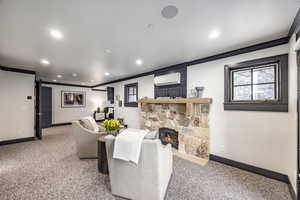 Living room featuring ornamental molding, a stone fireplace, carpet floors, and a wall mounted air conditioner