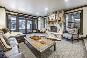 Carpeted living room with crown molding, a stone fireplace, and french doors