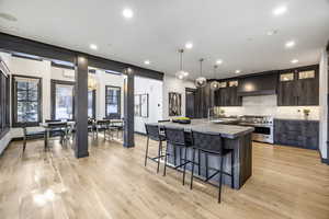 Kitchen featuring a breakfast bar, dark brown cabinets, double oven range, wall chimney range hood, and backsplash