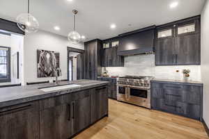 Kitchen featuring sink, dark brown cabinets, double oven range, custom range hood, and pendant lighting