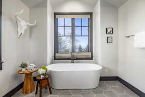 Bathroom with tile patterned flooring, vaulted ceiling, and a washtub