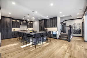 Kitchen featuring light hardwood / wood-style flooring, pendant lighting, dark brown cabinets, and an island with sink