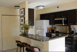 Kitchen with dark stone countertops, a kitchen breakfast bar, kitchen peninsula, and white fridge