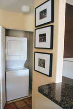 Laundry area with stacked washer and dryer and dark tile patterned flooring