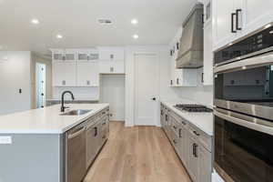 Kitchen with premium range hood, white cabinetry, sink, a kitchen island with sink, and stainless steel appliances