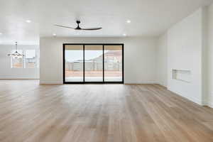 Unfurnished living room with ceiling fan with notable chandelier and light wood-type flooring