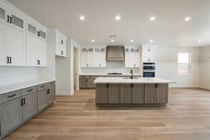 Kitchen with premium range hood, double oven, sink, gray cabinetry, and a large island with sink