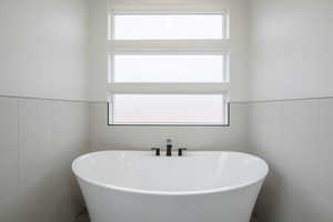 Bathroom featuring a healthy amount of sunlight, a tub to relax in, and tile walls