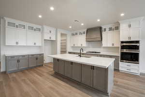 Kitchen with a center island with sink, white cabinets, and premium range hood