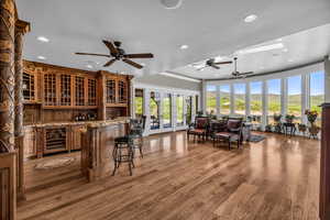 Interior space with wine cooler, ceiling fan, wood-type flooring, and light stone countertops