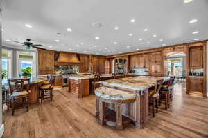 Kitchen featuring backsplash, a kitchen breakfast bar, high end stove, custom range hood, and a large island with sink