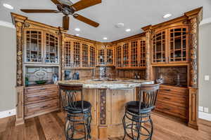 Kitchen featuring a kitchen bar, ornamental molding, kitchen peninsula, light stone countertops, and light wood-type flooring