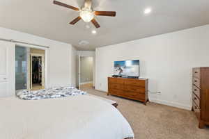 Bedroom with a walk in closet, vaulted ceiling, light colored carpet, and ceiling fan