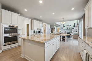 Kitchen featuring pendant lighting, white cabinetry, light stone countertops, and double oven