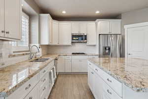 Kitchen featuring white cabinetry, appliances with stainless steel finishes, sink, and light stone counters