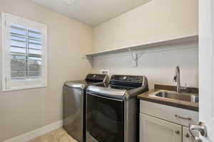 Washroom with sink, light tile patterned floors, washer and clothes dryer, and cabinets