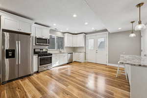 Kitchen with stainless steel appliances, white cabinetry, pendant lighting, and light stone counters