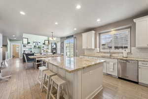 Kitchen featuring a kitchen island, decorative light fixtures, white cabinetry, dishwasher, and sink