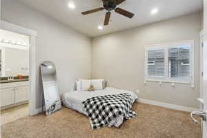 Bedroom with ceiling fan, connected bathroom, sink, and light carpet