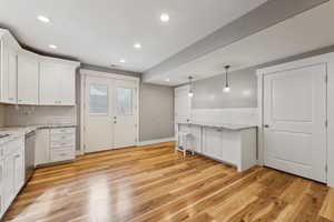 Kitchen with light hardwood / wood-style flooring, dishwasher, white cabinetry, hanging light fixtures, and light stone counters