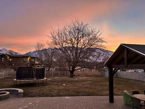 Yard at dusk featuring a trampoline, a gazebo, a patio, a storage unit, and a mountain view