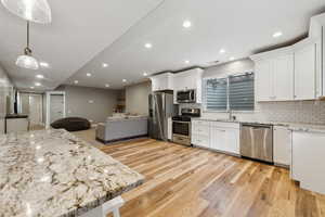 Kitchen with appliances with stainless steel finishes, decorative light fixtures, white cabinetry, sink, and light wood-type flooring