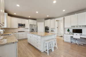 Kitchen featuring sink, white cabinetry, stainless steel appliances, light stone countertops, and a kitchen island