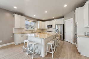 Kitchen with white cabinetry, a breakfast bar area, stainless steel appliances, and a center island