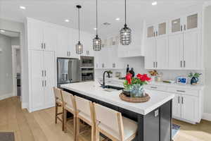 Kitchen featuring stainless steel appliances, white cabinets, and a center island with sink