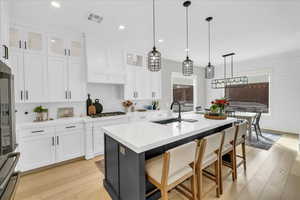 Kitchen featuring sink, stainless steel gas cooktop, white cabinetry, a center island with sink, and pendant lighting