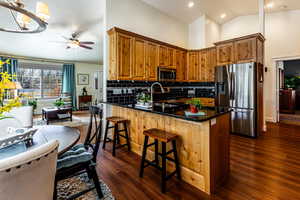 Kitchen featuring appliances with stainless steel finishes, decorative backsplash, ceiling fan, kitchen peninsula, and dark wood-type flooring