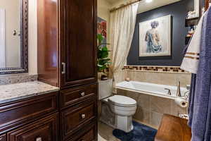 Bathroom with vanity, tiled bath, tile patterned floors, and toilet