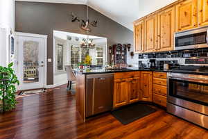 Kitchen with pendant lighting, appliances with stainless steel finishes, decorative backsplash, vaulted ceiling, and kitchen peninsula